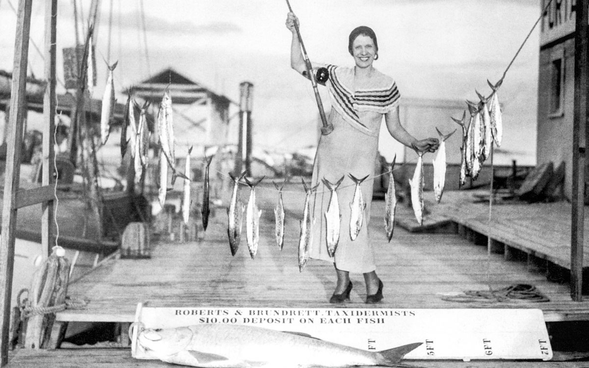 Aimee McPherson, idressed in a dress, stands with a string of fish.