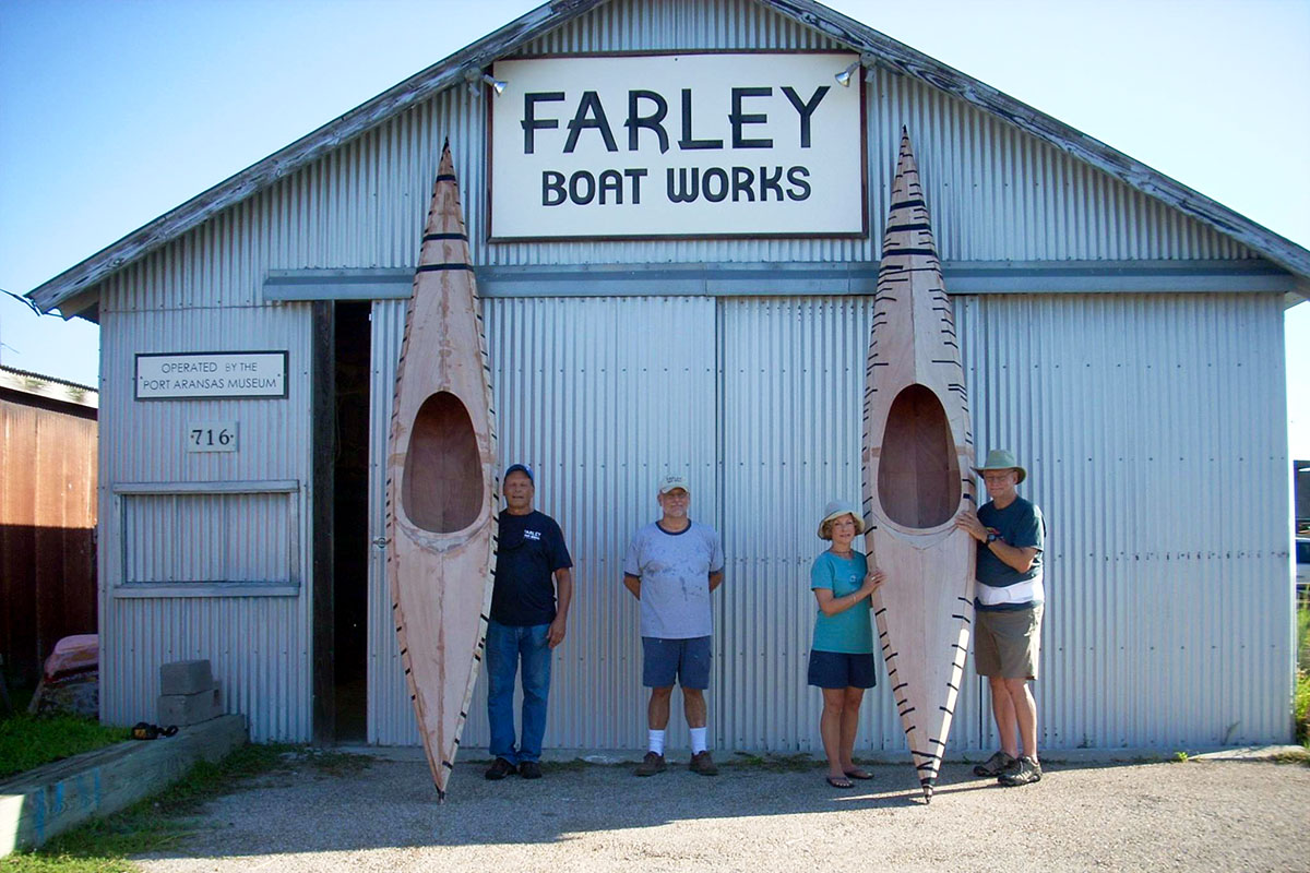 People standing in front of Farley Boat Works with two unfinished kayaks.
