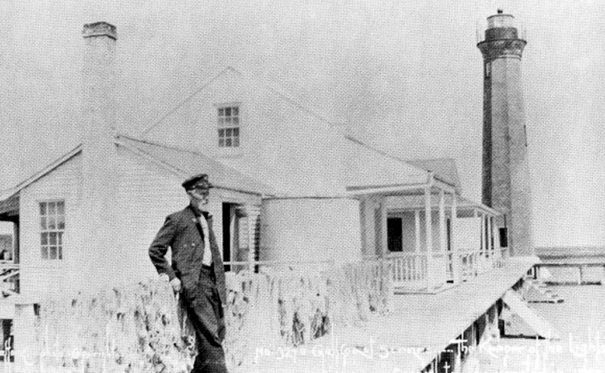 Vintage photo of a lighthouse keeper in uniform standing near the lighthouse.