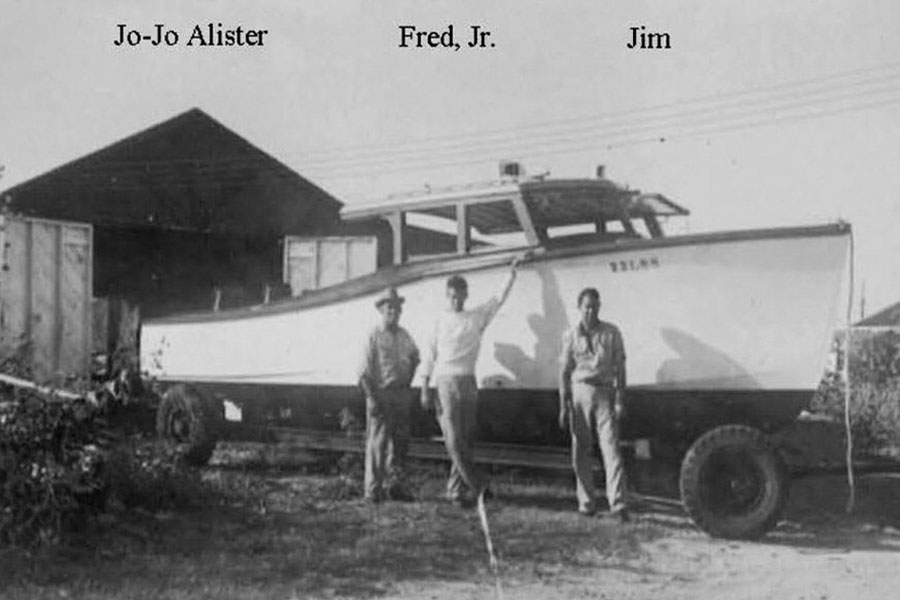Three men standing near a boat in front of Farley Boat Works