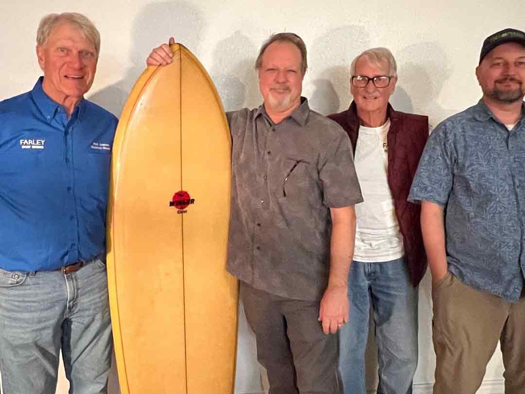 Dan Parker and 3 other men pose with a surfboard