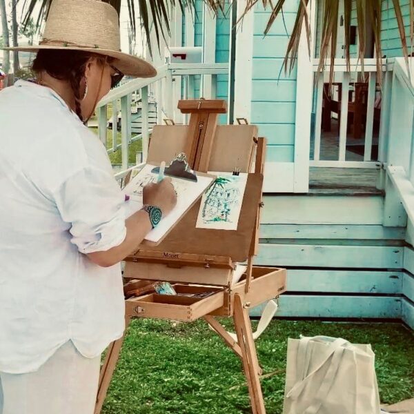 Woman painting on an easel in front of a turquoise house
