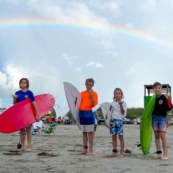 Kids on beach holding surfboards with rainbow in background